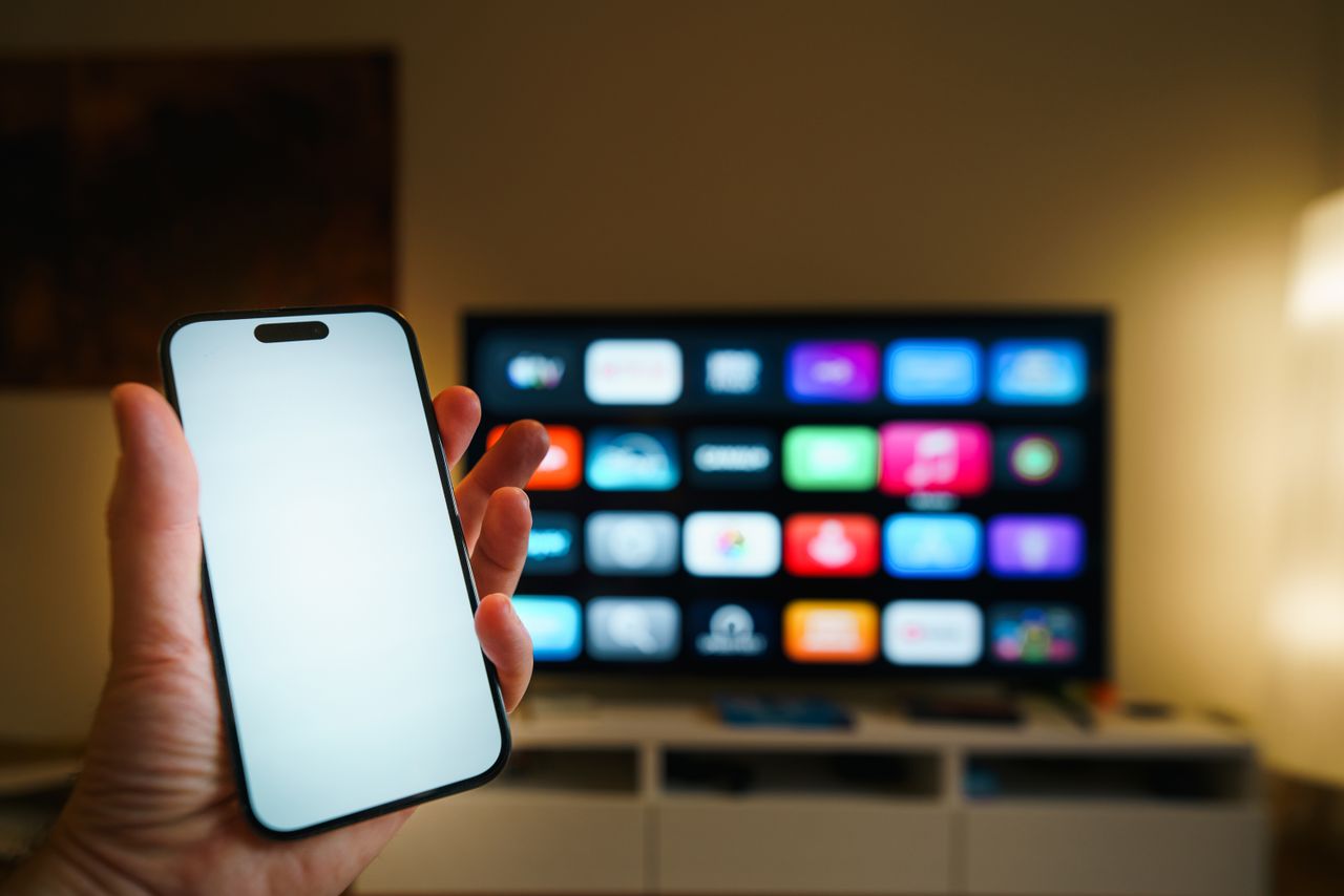 The Art of Drawing Readers In: Your attractive post title goes here A smartphone in focus with a smart TV displaying apps in a cozy living room.